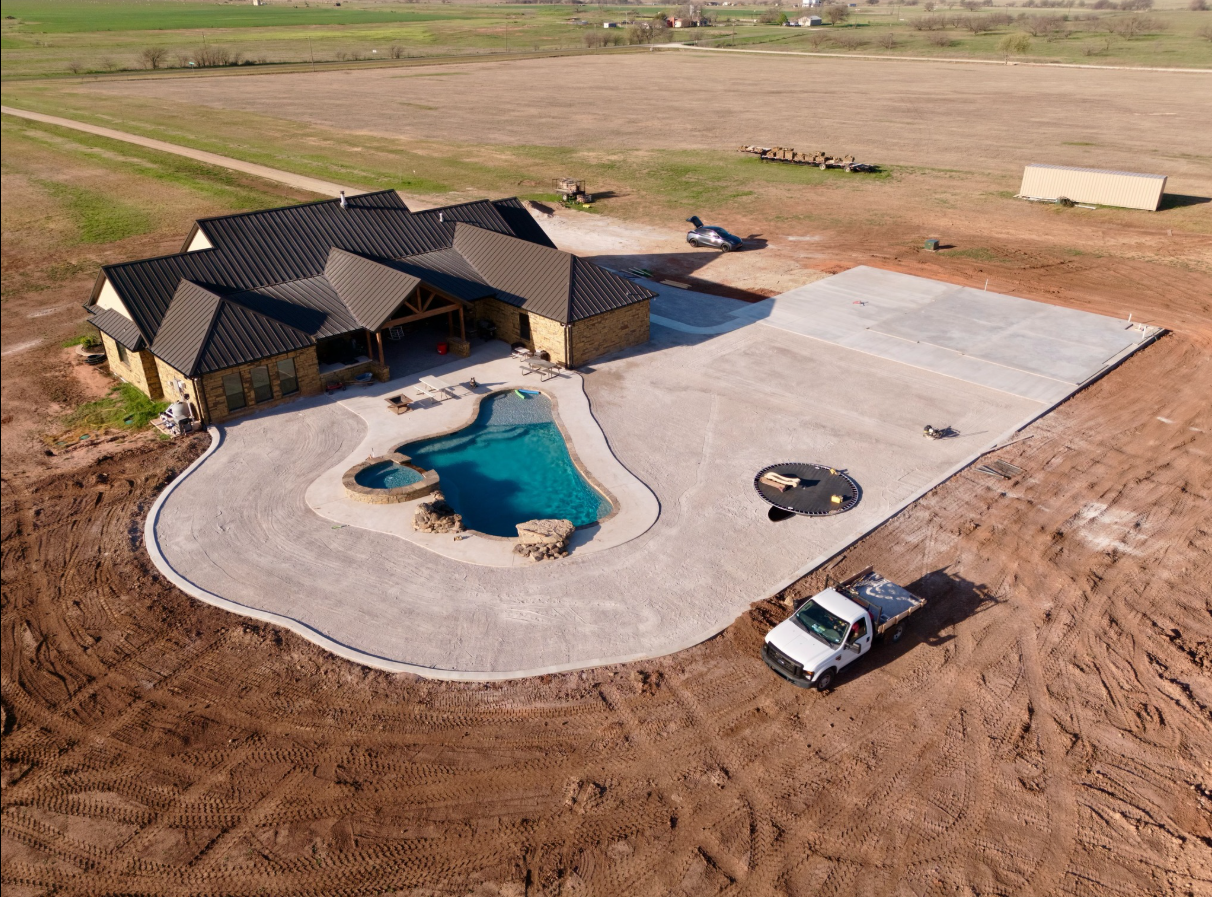 Aerial view of a home with a pool, driveway, and dirt construction site. White truck in the foreground.
