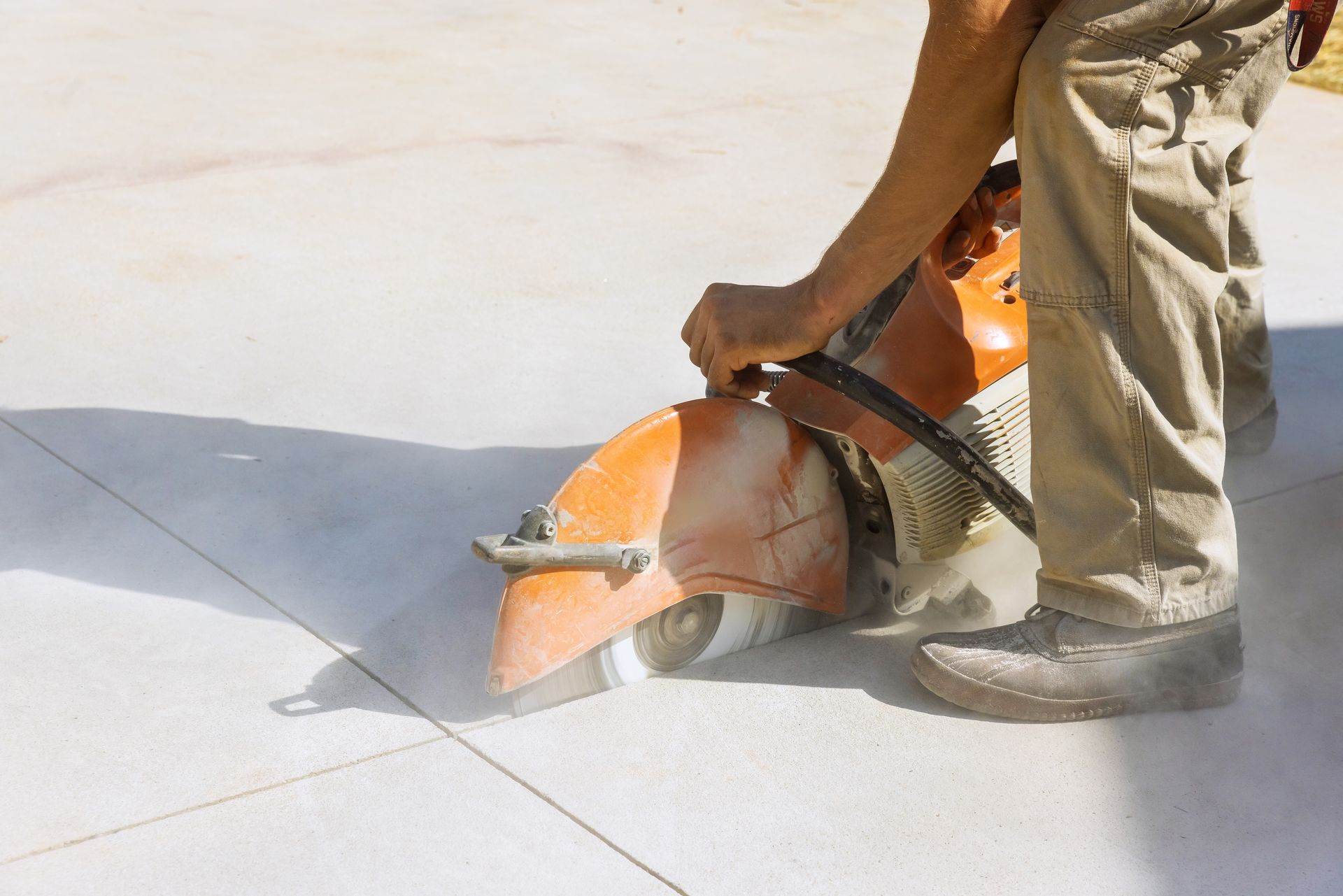 Person cutting concrete with a power saw, creating dust.