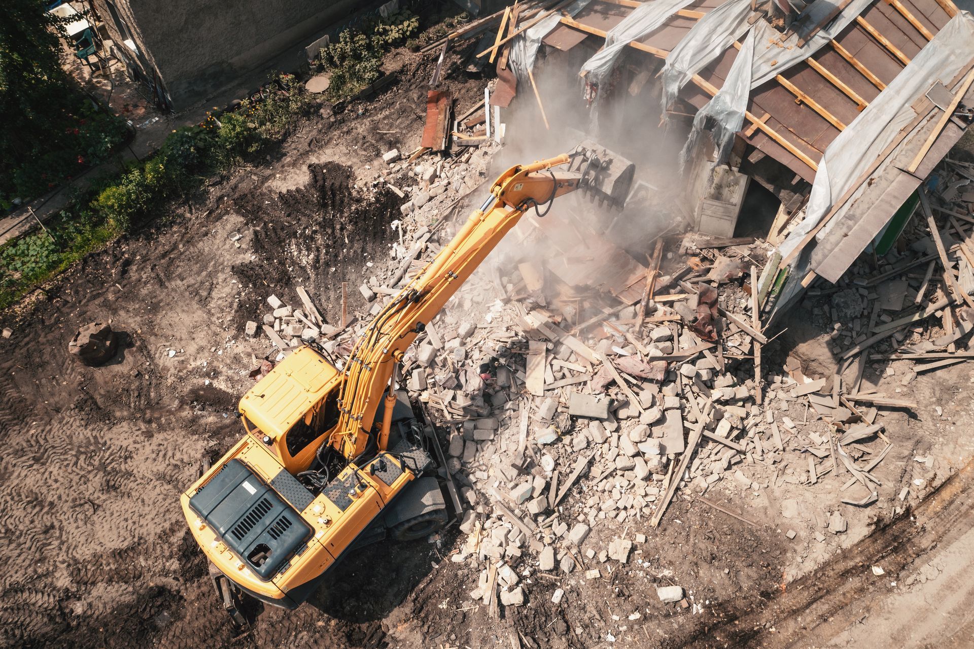 Yellow excavator demolishing a building, kicking up dust and debris.
