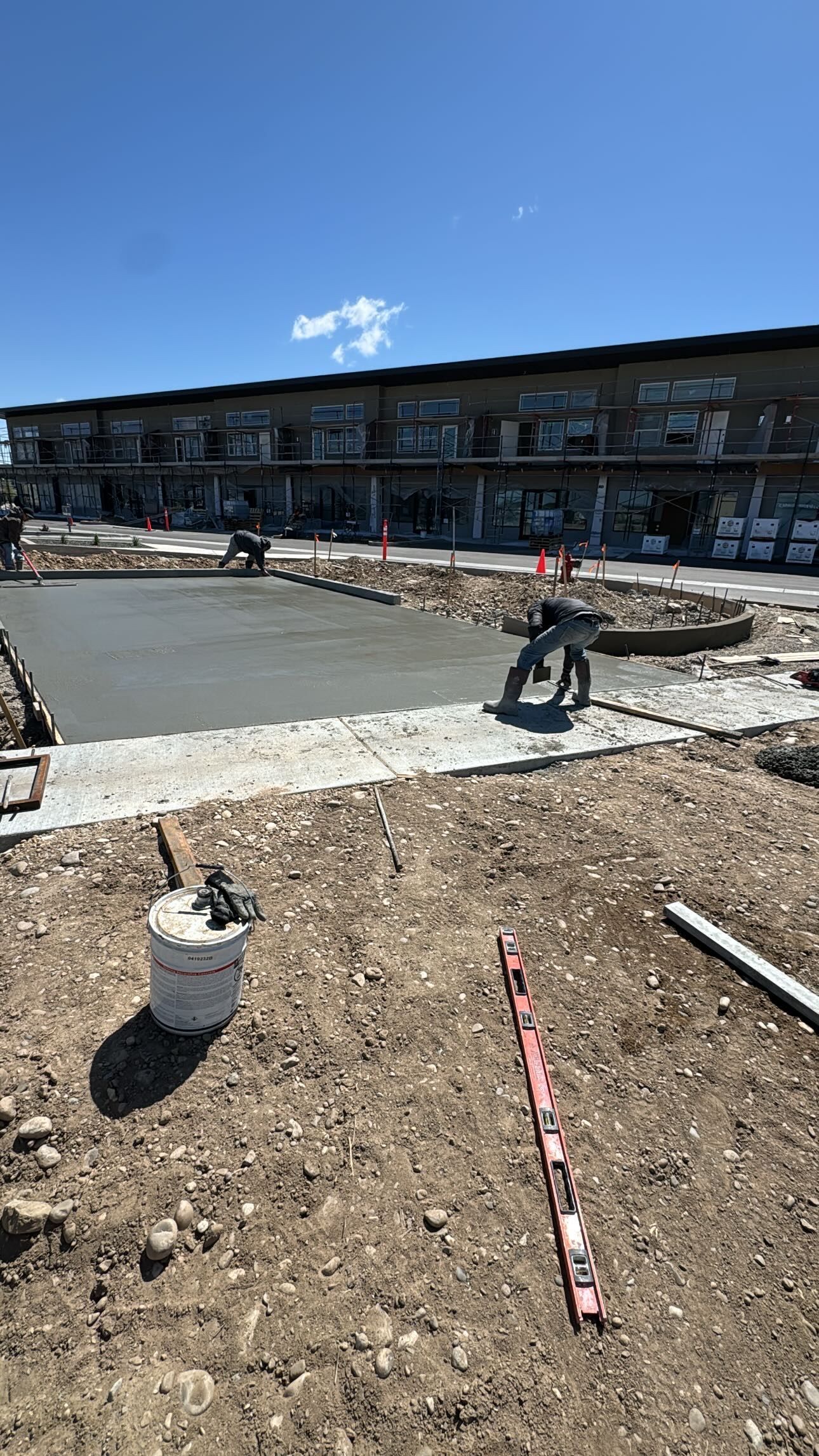 Construction site with freshly poured concrete slab; building in background.