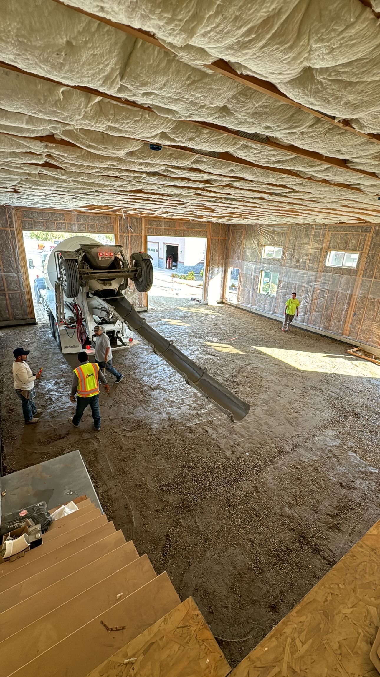 Construction site: workers pouring concrete on a floor with a pump truck.
