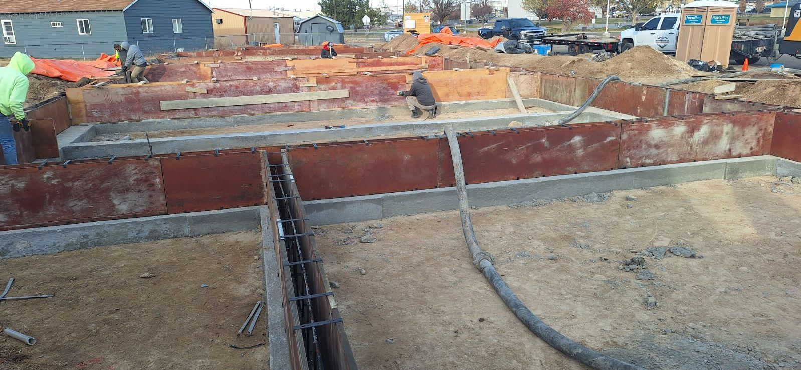 Construction site with a partially built foundation. Workers are present, and a concrete hose is visible.