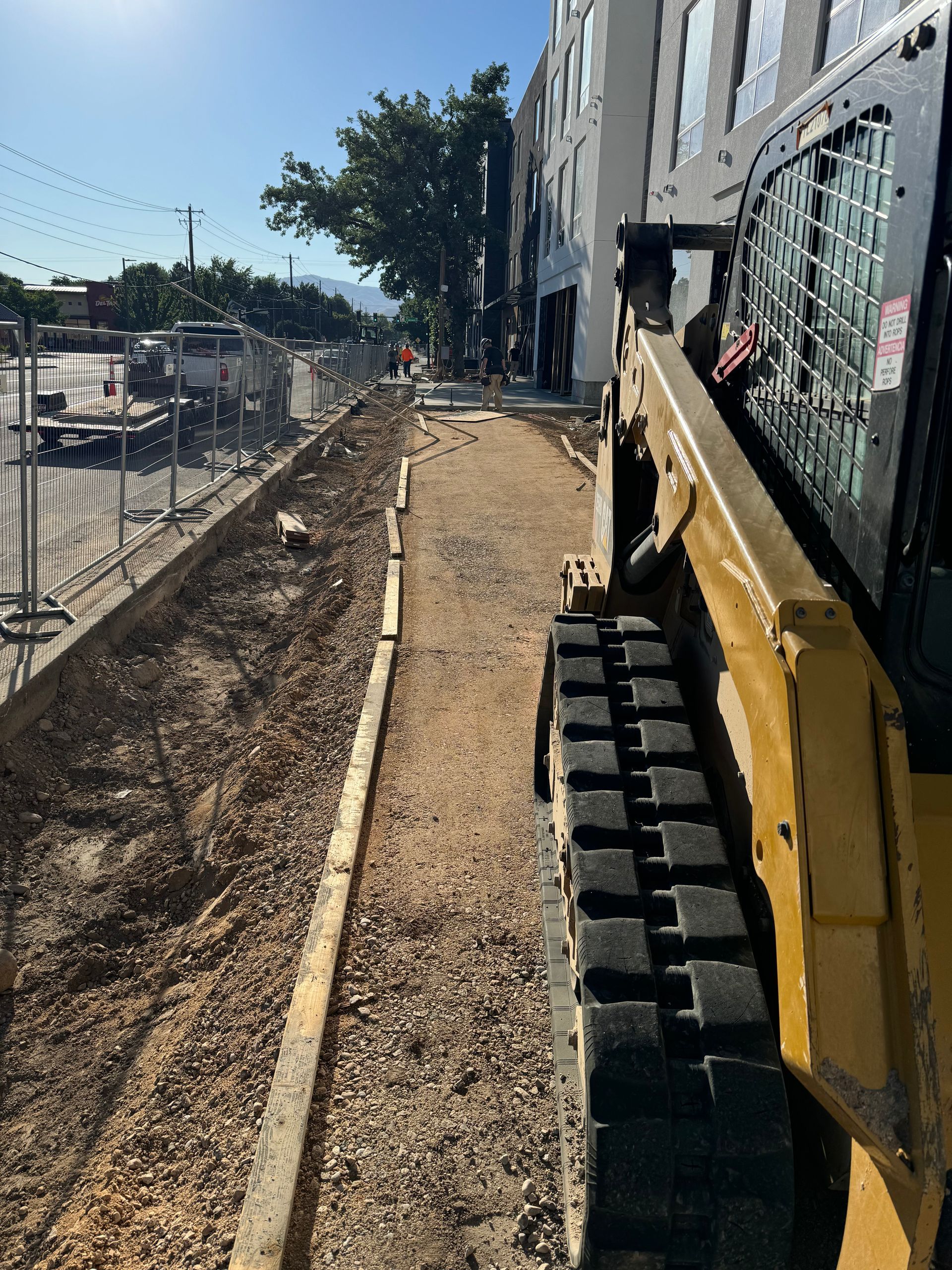 Construction site with a yellow track loader. A gravel path is being laid next to a fence and building.