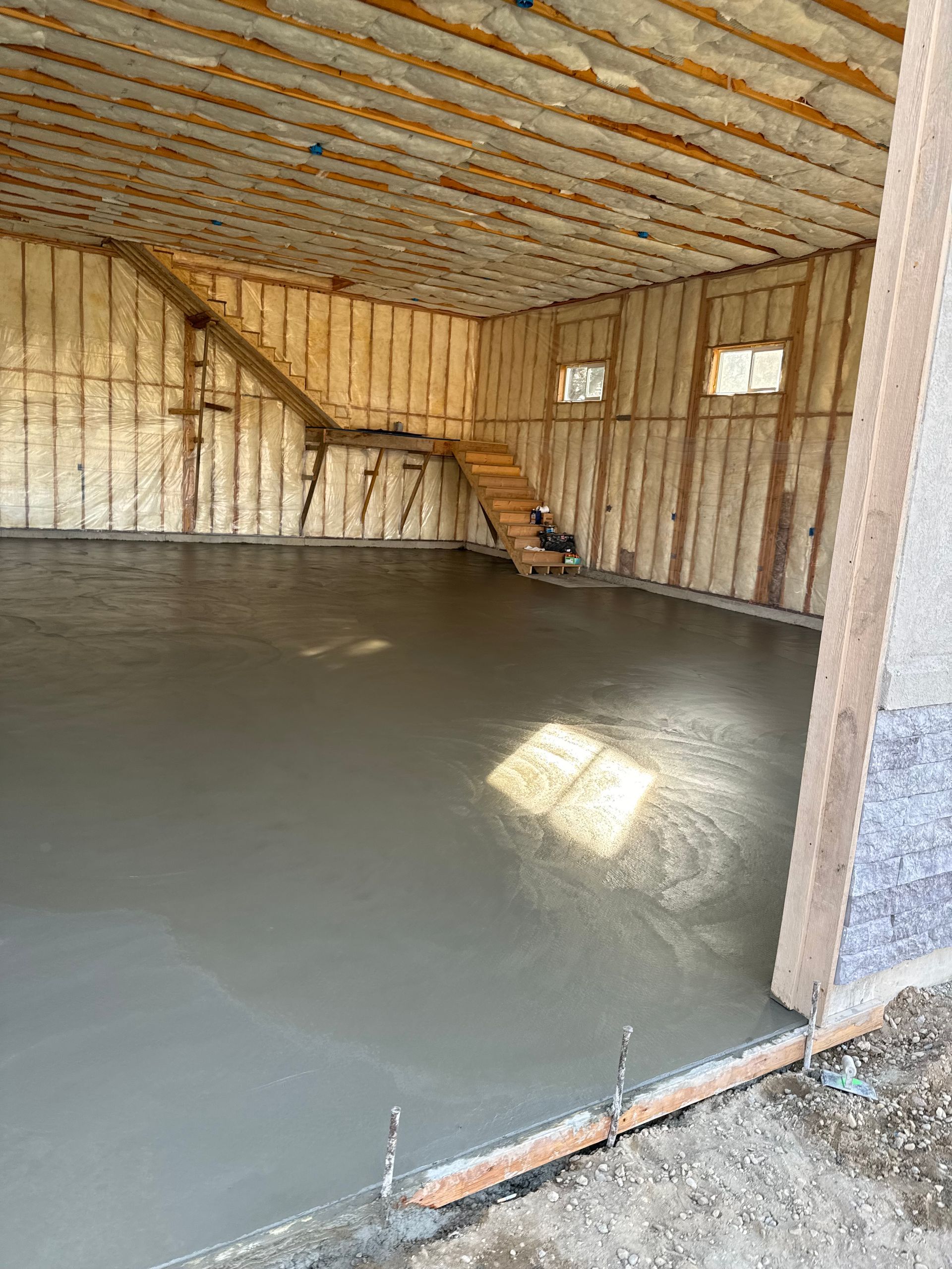 Interior of a new building, with a smooth, gray concrete floor. Wooden frame walls and ceiling, stairs visible.