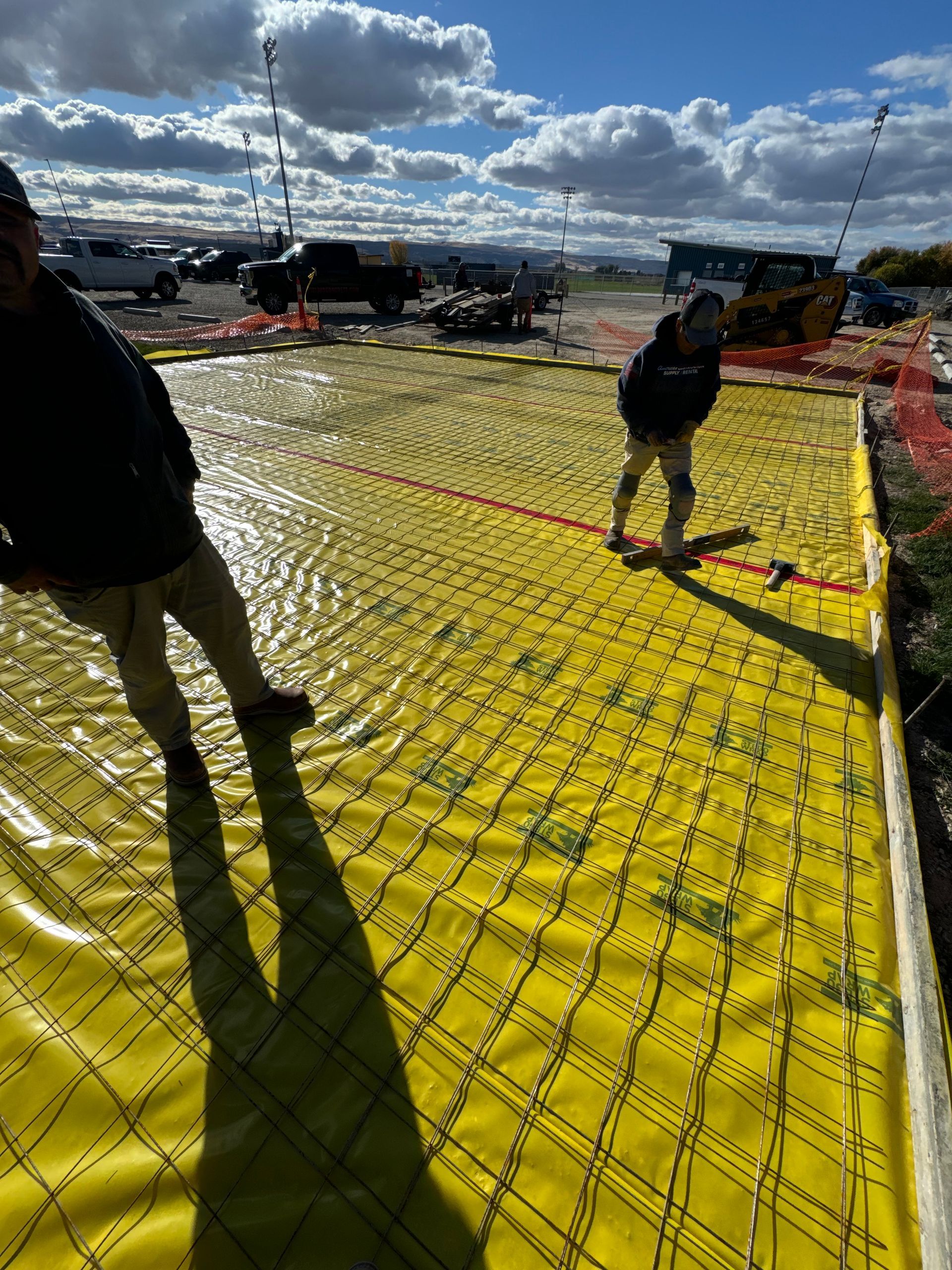 Two workers on yellow grid fabric, laying concrete, outdoor setting.