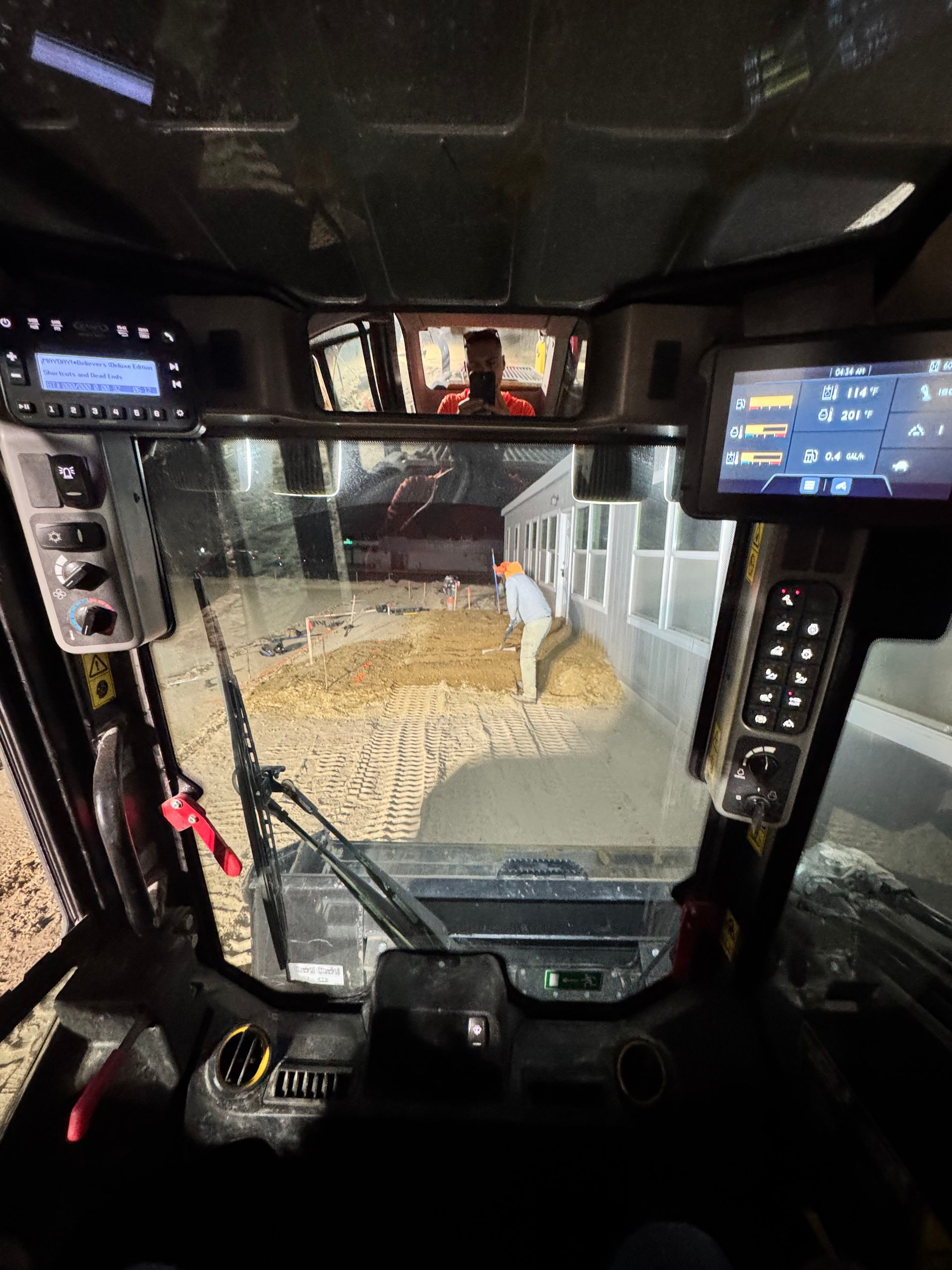 View from inside a skid steer loader; a person is outside, working near a building with feed.