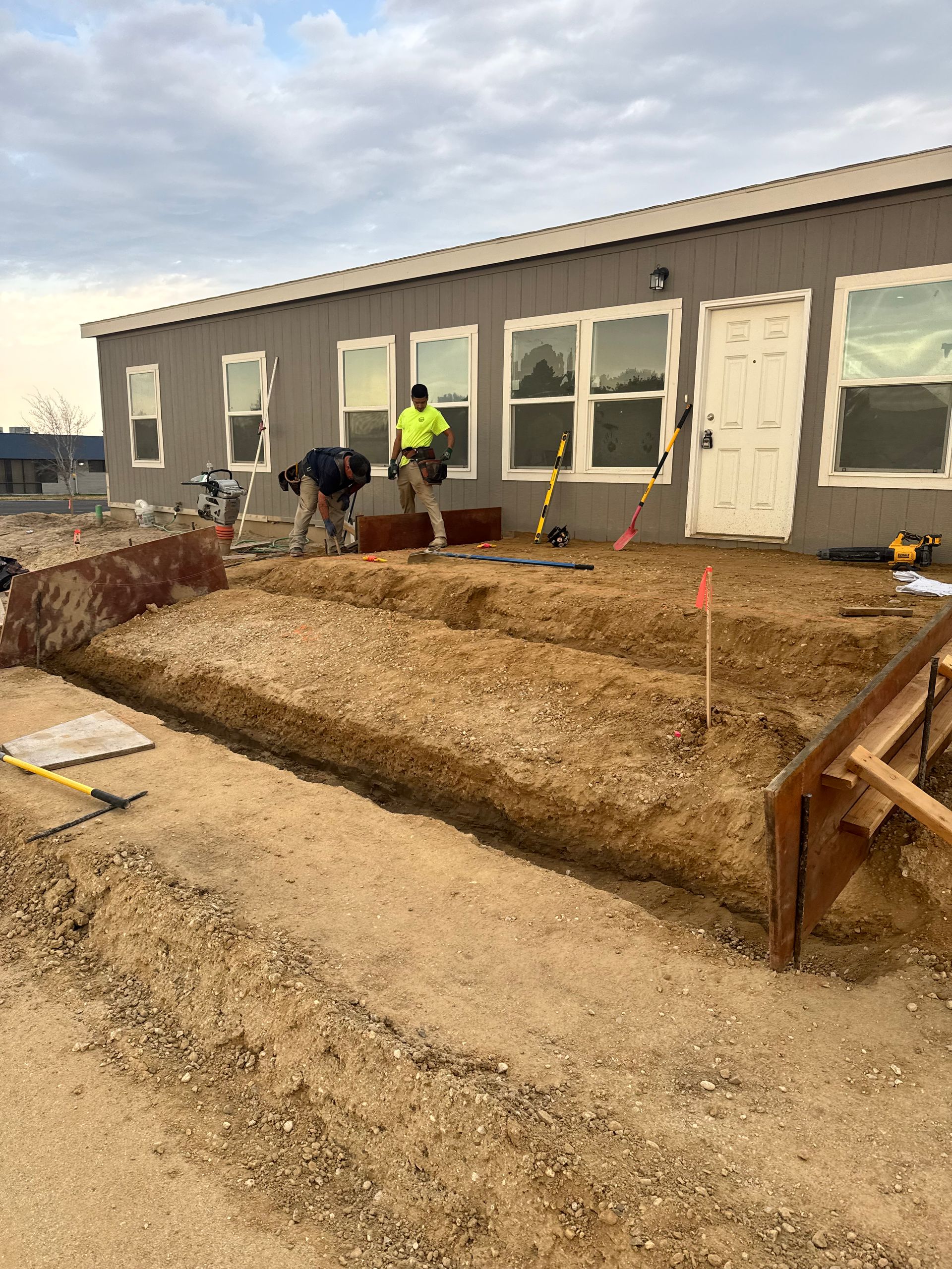 Construction workers digging near a building with windows, dirt and tools present.