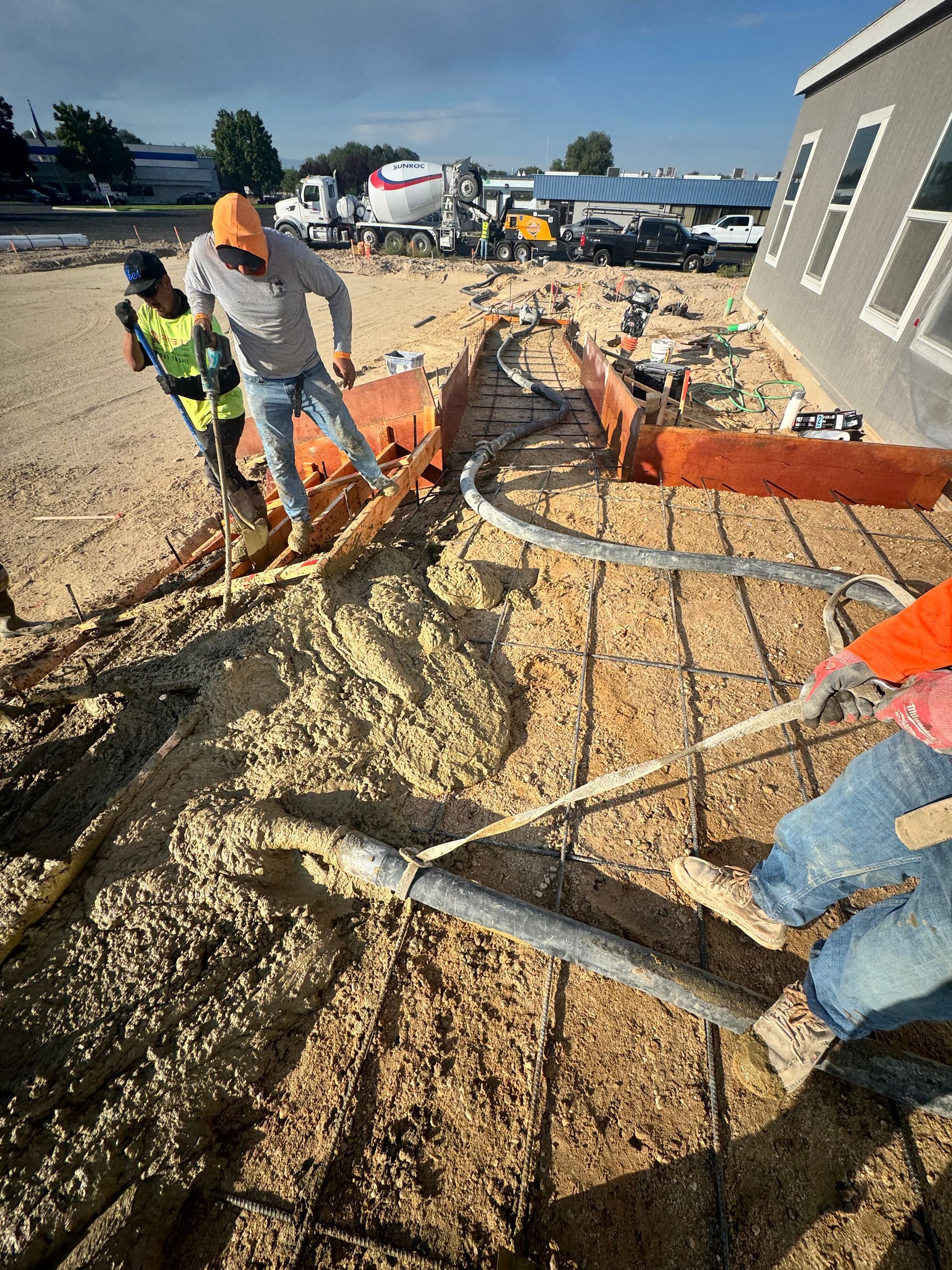 Construction workers pouring concrete at a building site; men wearing hard hats and safety vests.