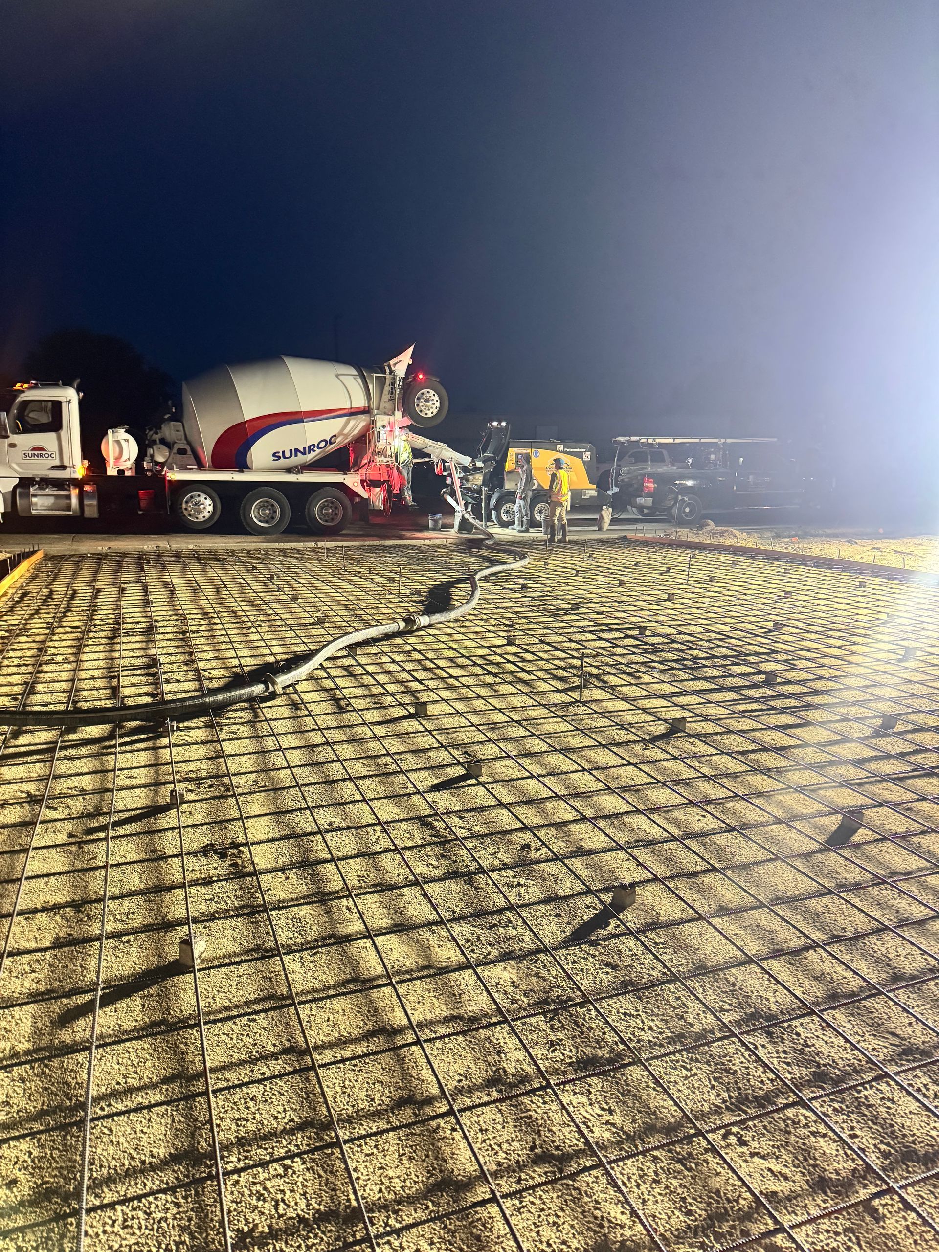 Concrete pour at night: cement truck pouring concrete over rebar grid on a construction site.