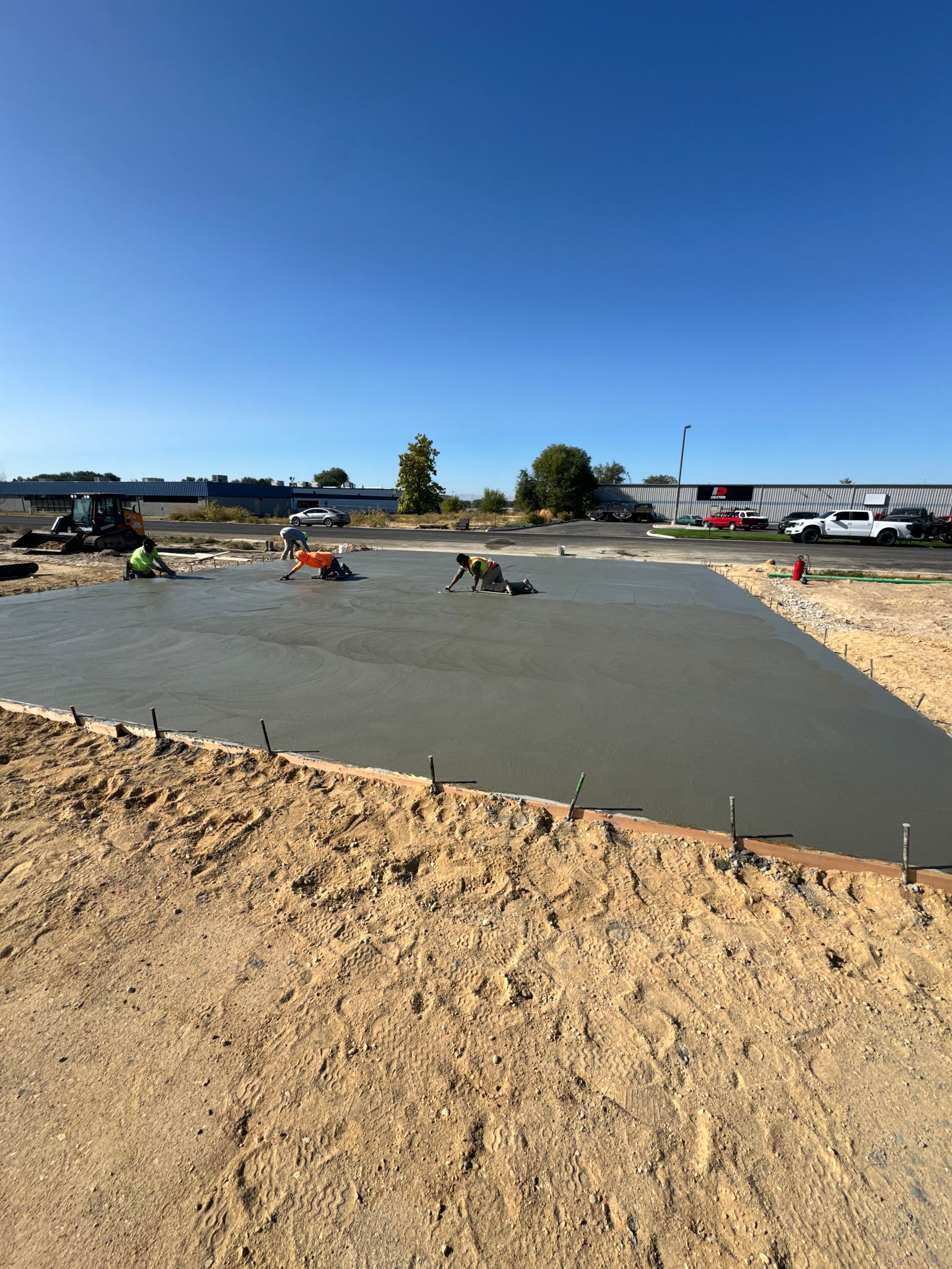 Construction workers smoothing fresh concrete slab on a sunny day.