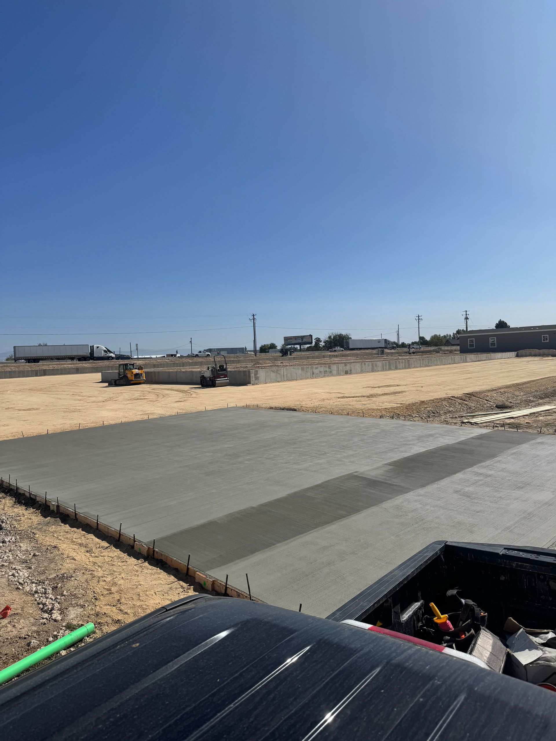 Construction site with fresh concrete slab, back of truck in foreground, blue sky.