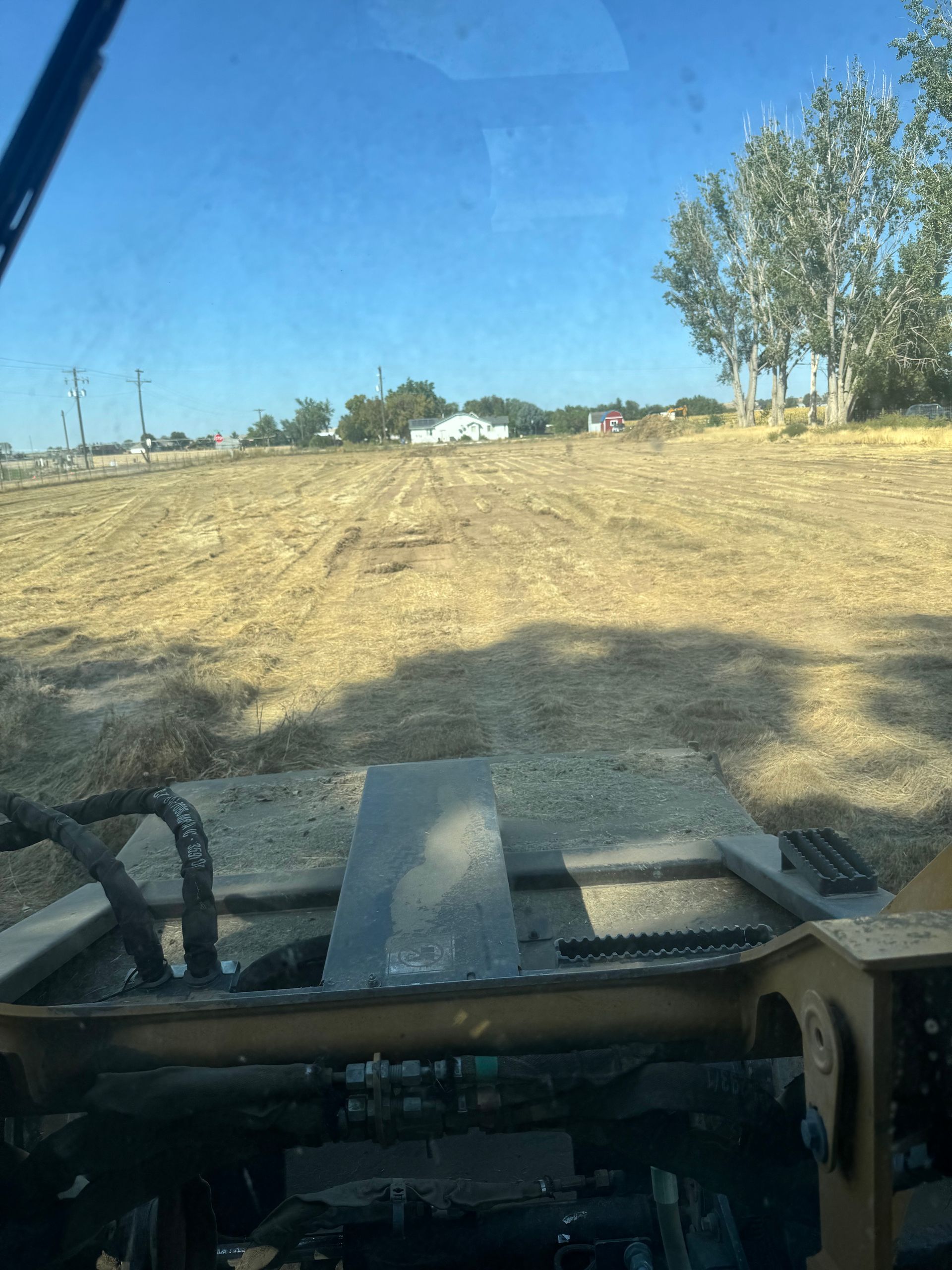 View from inside a machine with a field in front, buildings and trees in the distance under a blue sky.