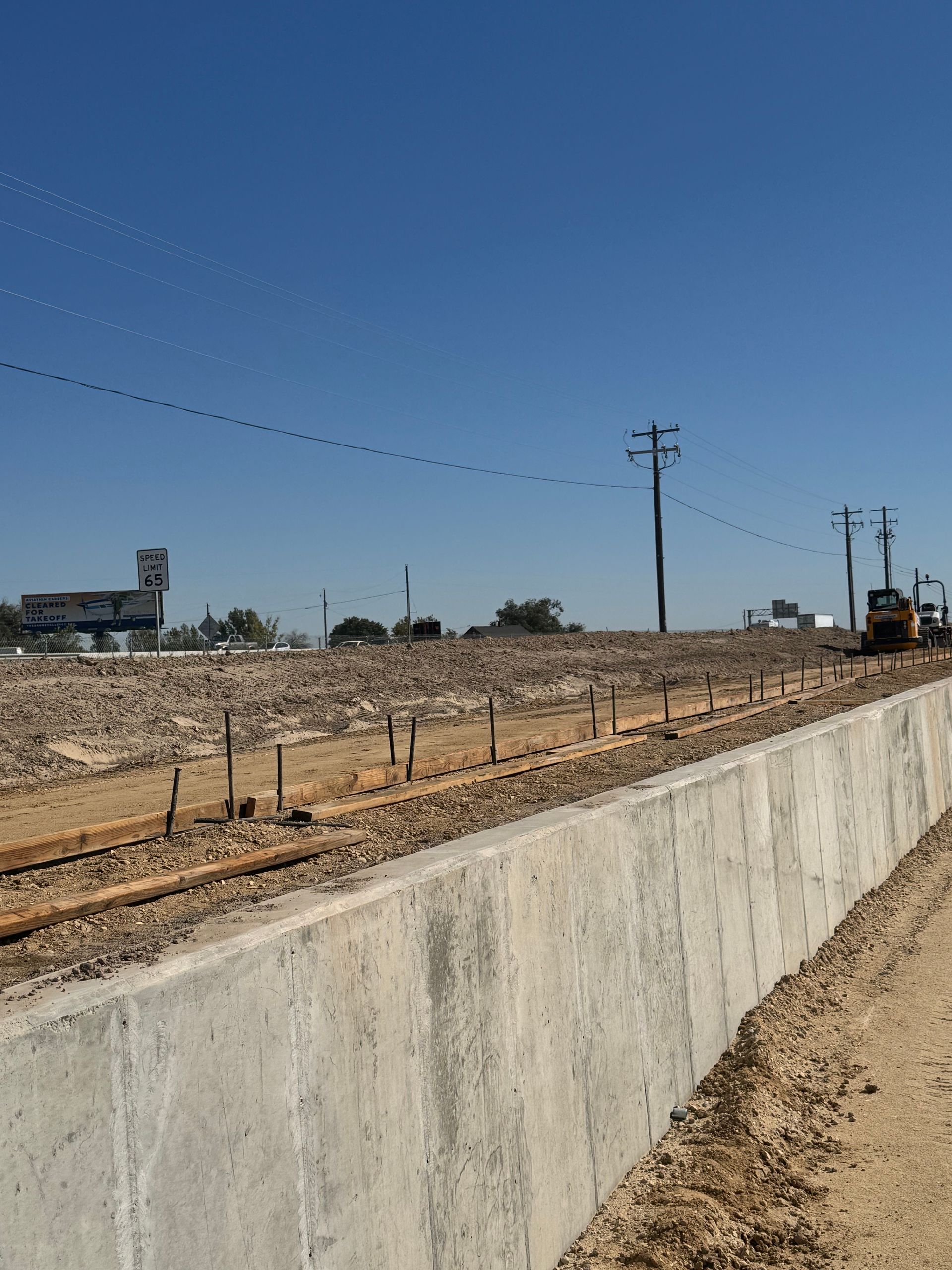 Construction site with concrete wall, railroad tracks, and heavy machinery under a blue sky.