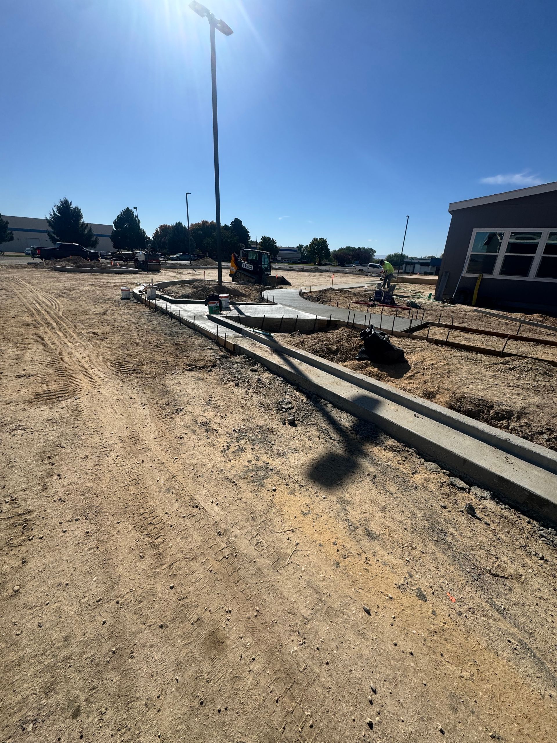 Construction site with newly poured concrete sidewalk. A light pole casts a shadow. Sunny day.