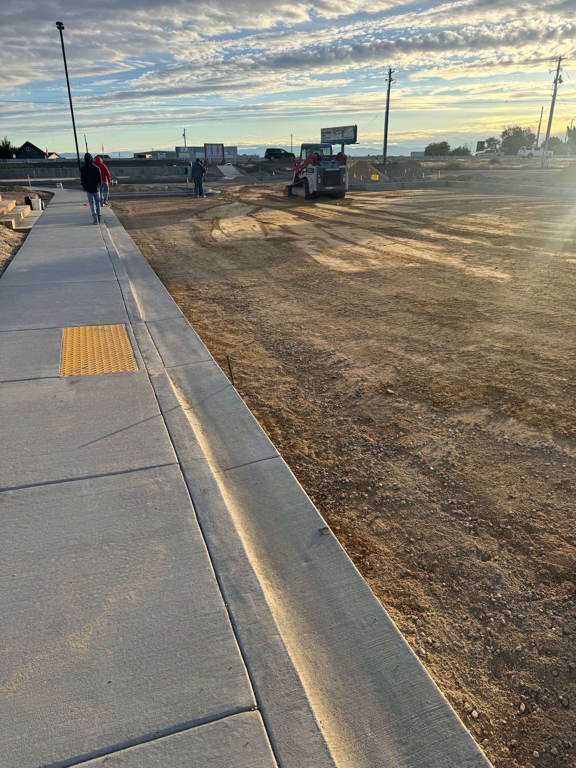 Sidewalk with tactile paving, construction site with worker, blue sky, morning sun.