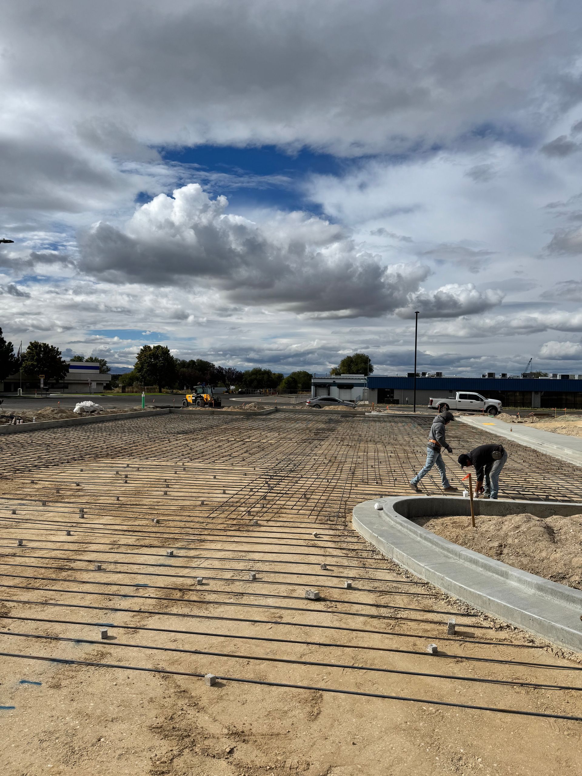 Construction site with workers laying down edging, dirt and cloudy sky.