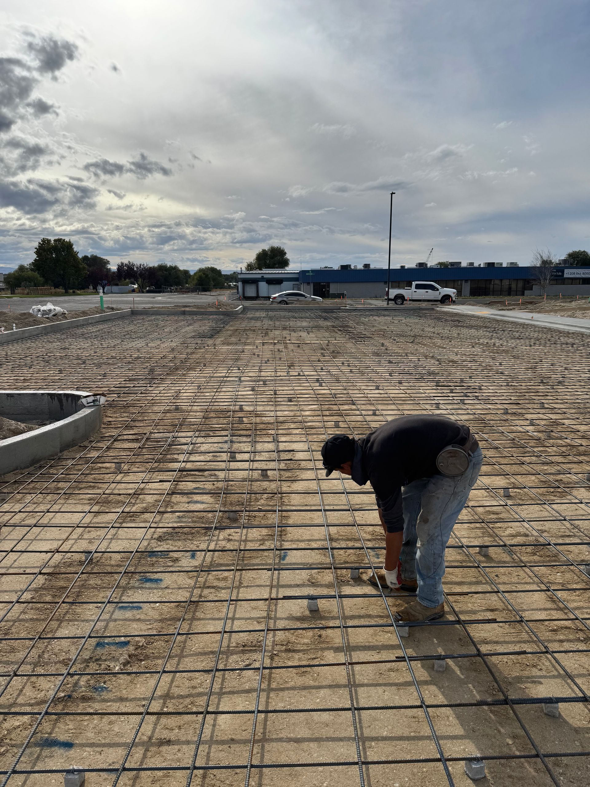 Man bends over rebar grid on a construction site, preparing for concrete pour.