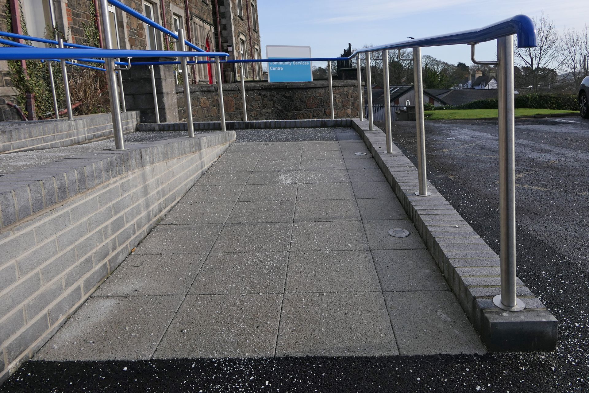 Ramp with blue handrails and gray brick, providing accessible entry to a building.