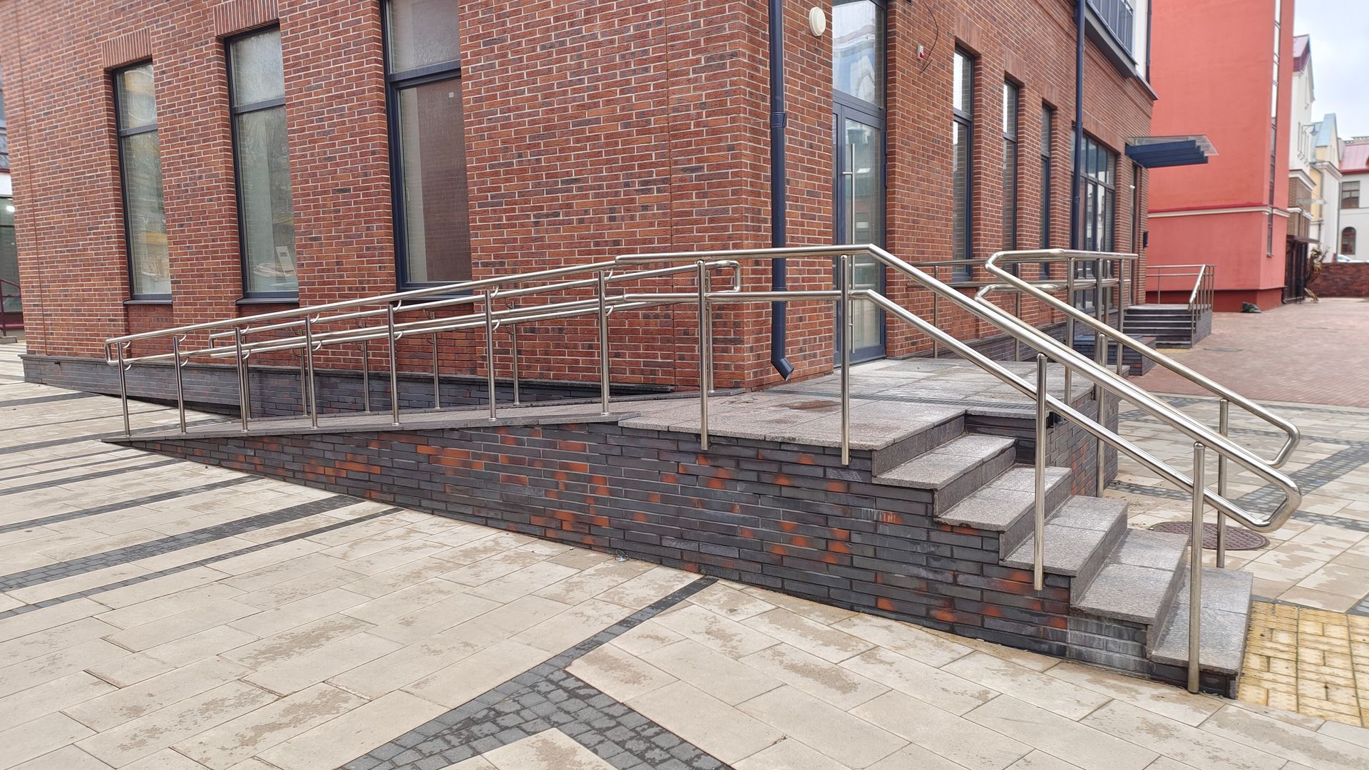 Brick building with ramp and stairs, metal railings, paved outdoor area.
