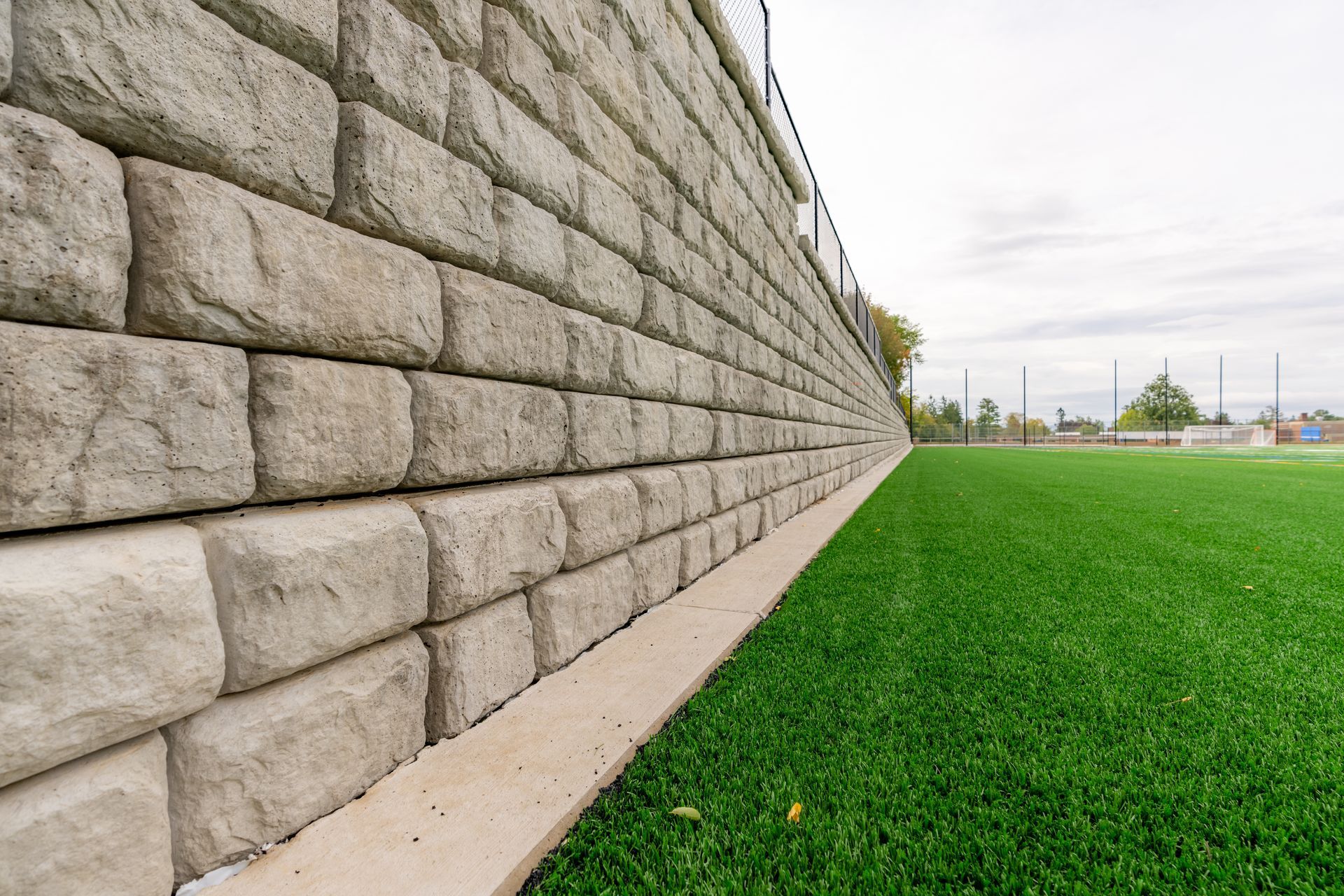Stone retaining wall bordering a green artificial turf field.