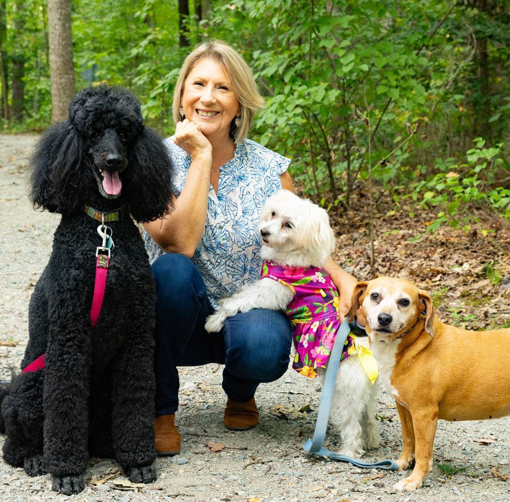 Woman with three dogs on a path. The woman is smiling, dogs are different sizes and colors.