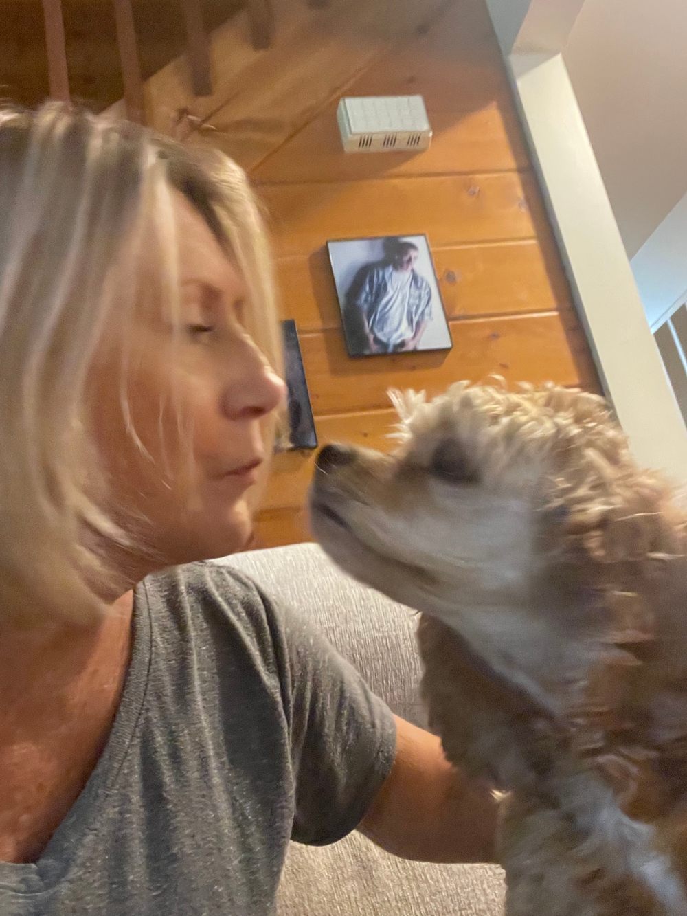 Blonde woman smiling, hugging a dog with gray and white fur, both looking at the camera.