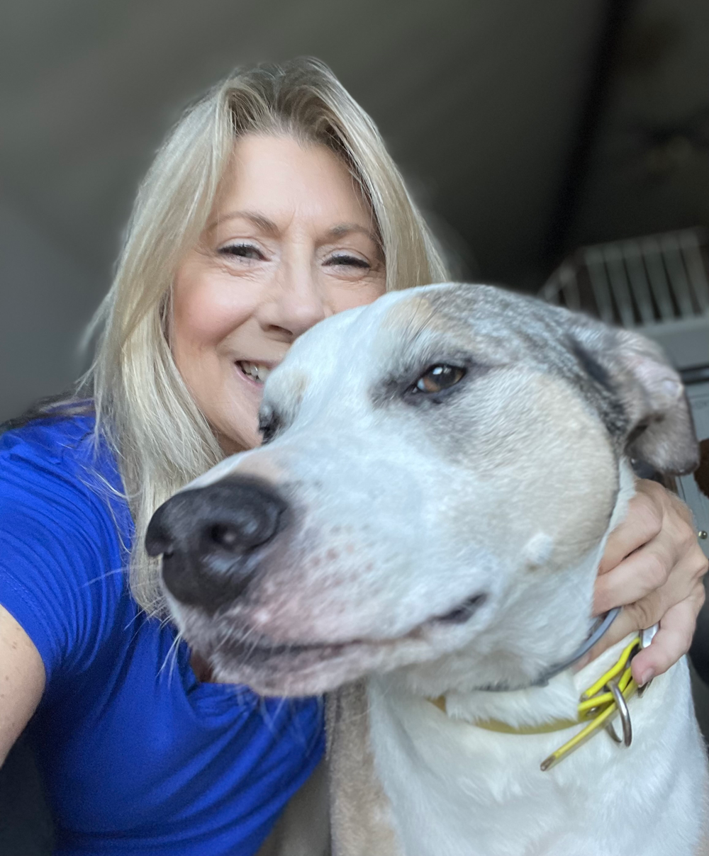 Woman in blue shirt smiling with a dog, both looking at the camera.