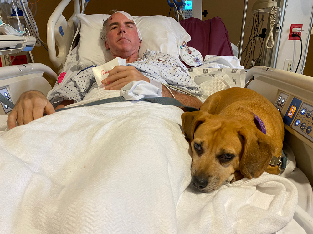 Man in hospital bed with dog; both appear to be resting.