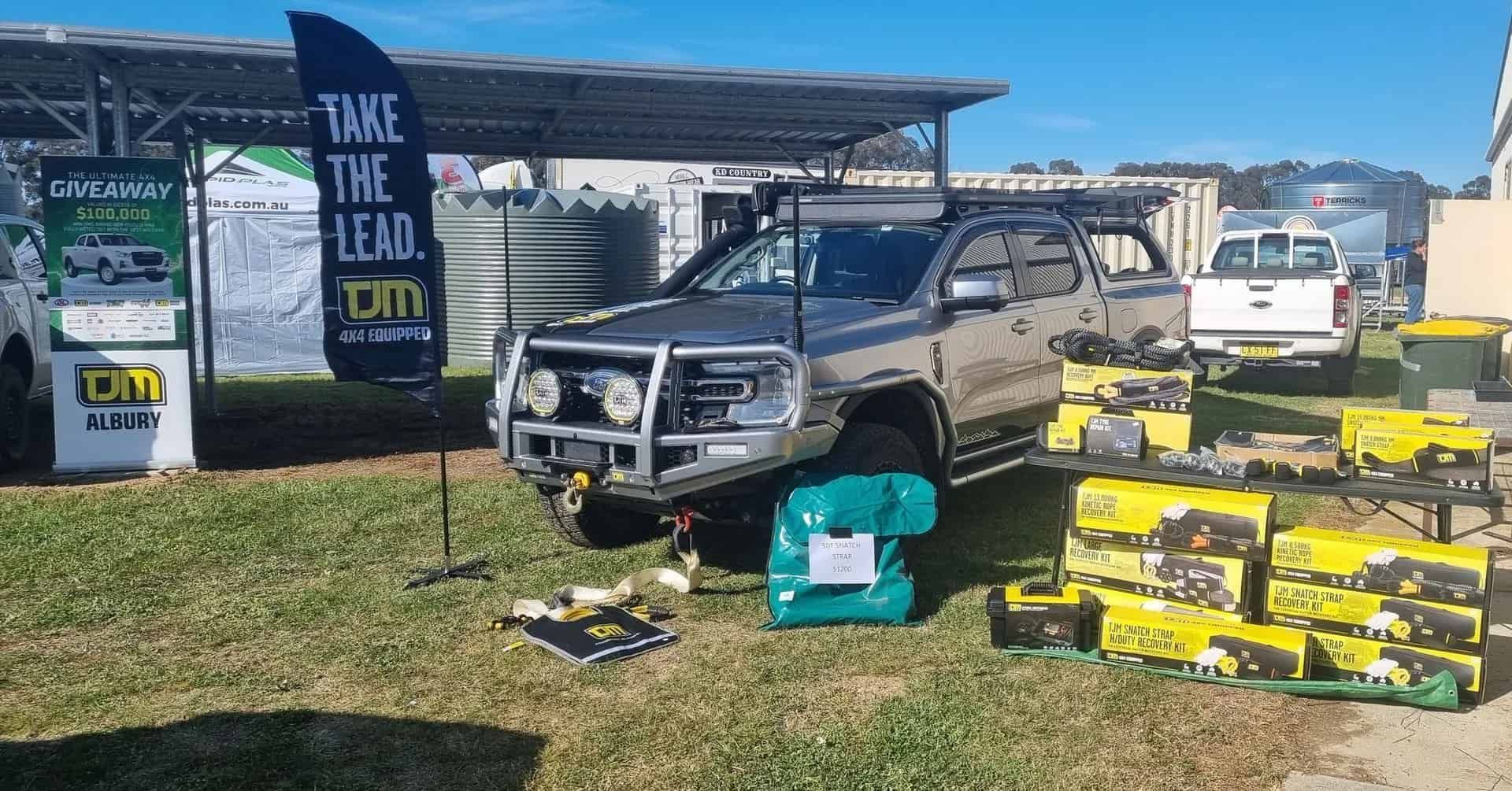 A display booth at an outdoor event featuring a modified truck, batteries, and promotional flags. — TJM Albury Pty Ltd in South Albury, NSW