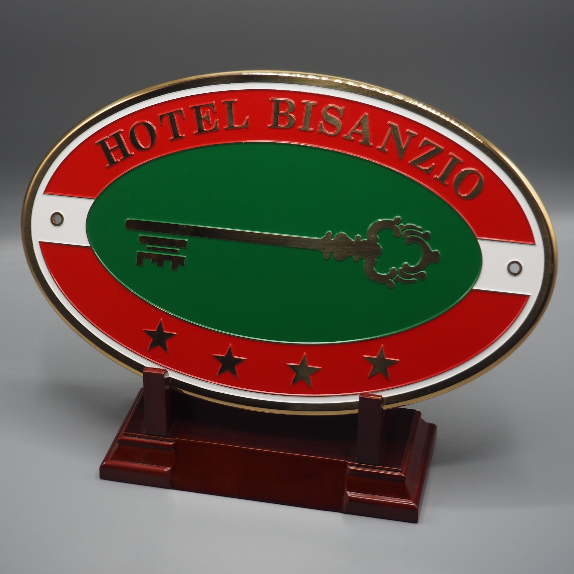 Insegna ovale dell'Hotel Bisanzio con l'icona di una chiave, quattro stelle dorate e colori rosso, verde e bianco su un supporto in legno.