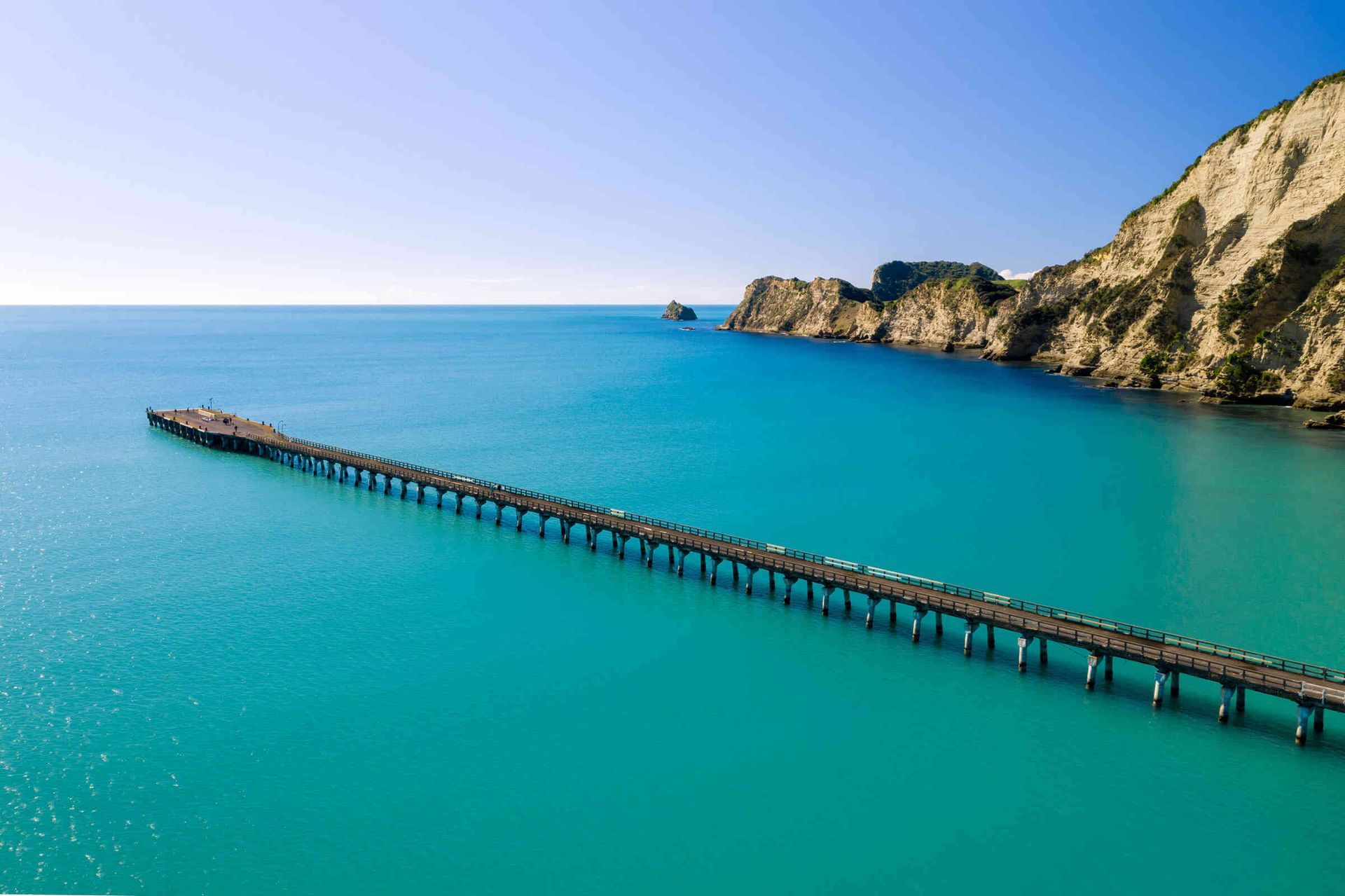Sunlit Tolaga Bay Wharf stretching into turquoise waters on New Zealand’s East Cape.