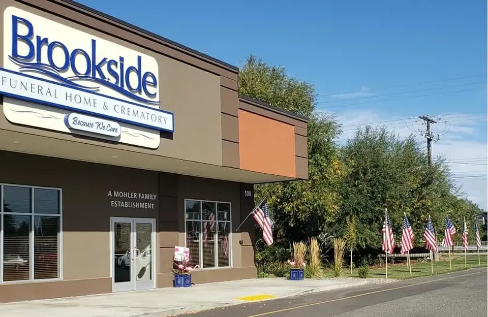 Brookside Funeral Home & Crematory, exterior view with American flags. Brown and tan building with blue sky.