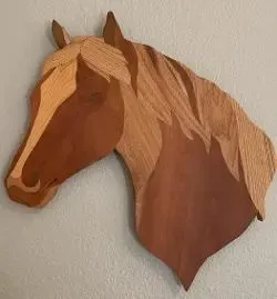 Wooden horse head sculpture, brown and tan, mounted on a white wall.