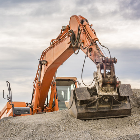 Frontal view of an orange excavator climbed on top of a ballast pile.