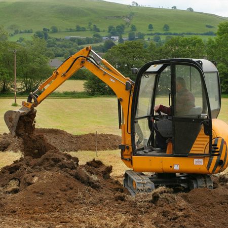 Mini digger moving earth in a field in rural countryside