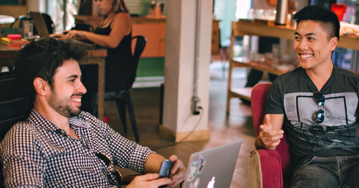 Two men are sitting in a chair with a laptop and talking to each other.