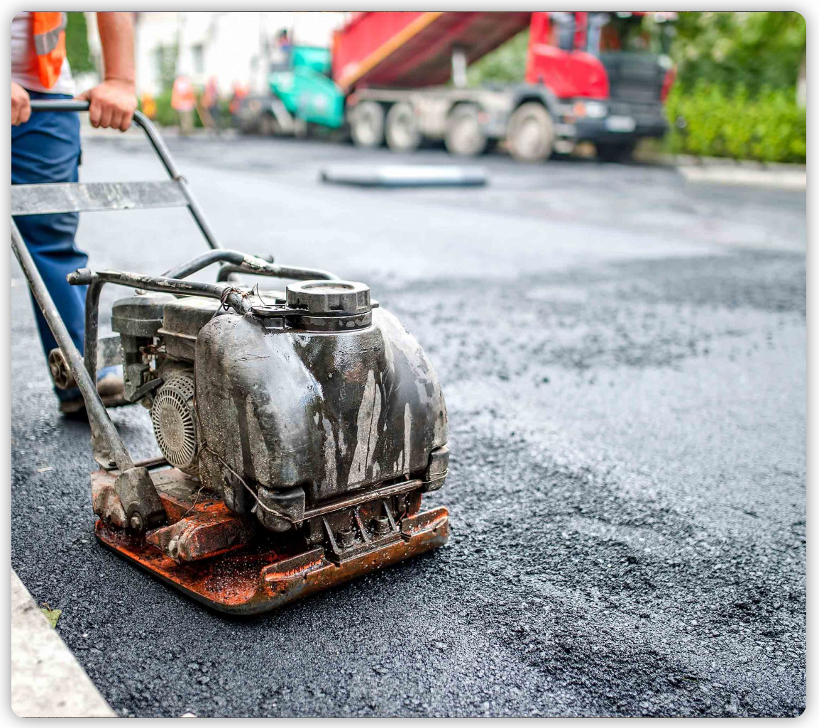 A man is using a machine to compact asphalt on a road.