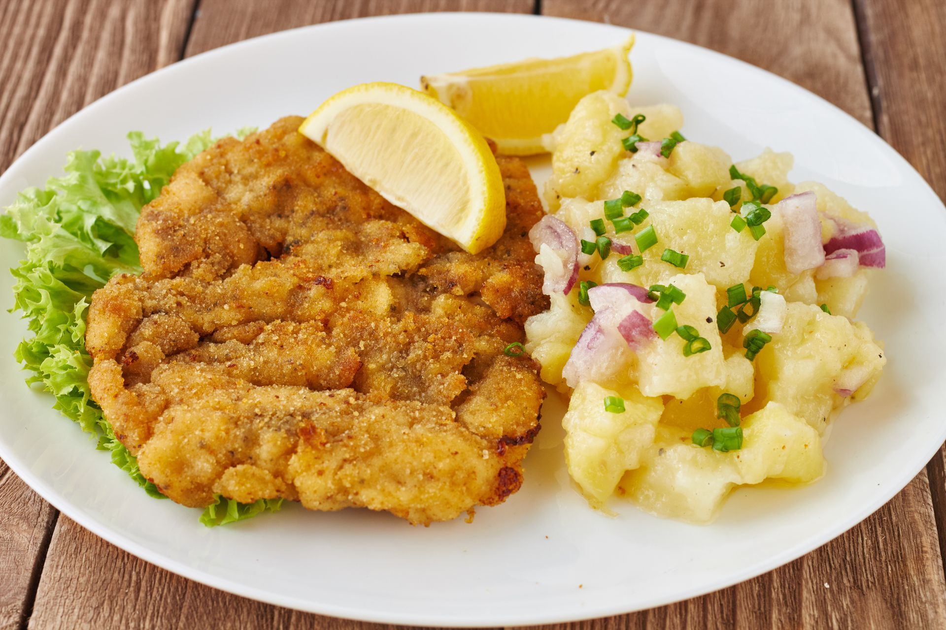 Paniertes Schnitzel mit Kartoffelsalat und Zitronenspalte auf einem weißen Teller.