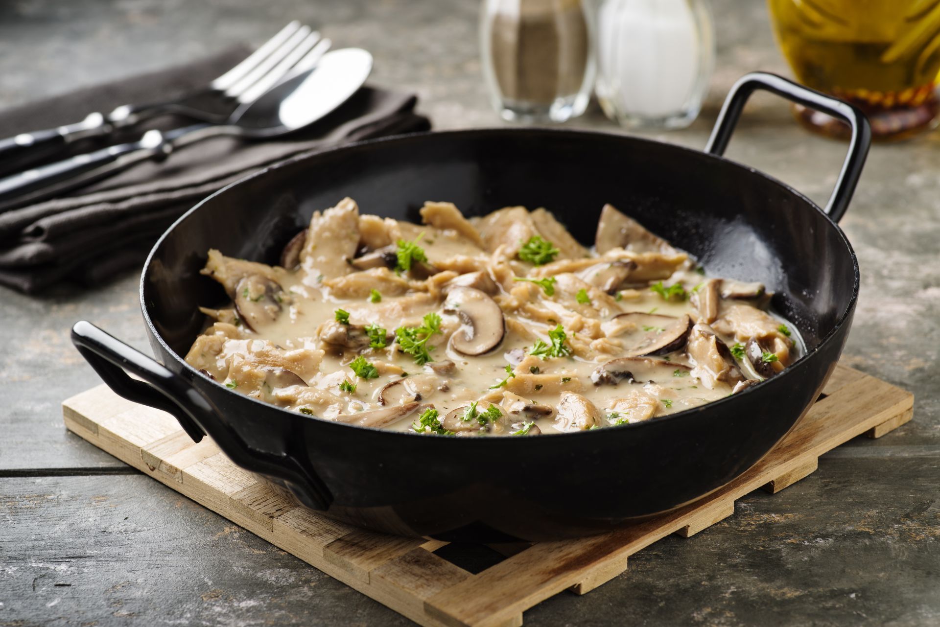 Hähnchen-Pilz-Gericht in einer schwarzen Pfanne auf einem Holzbrett.