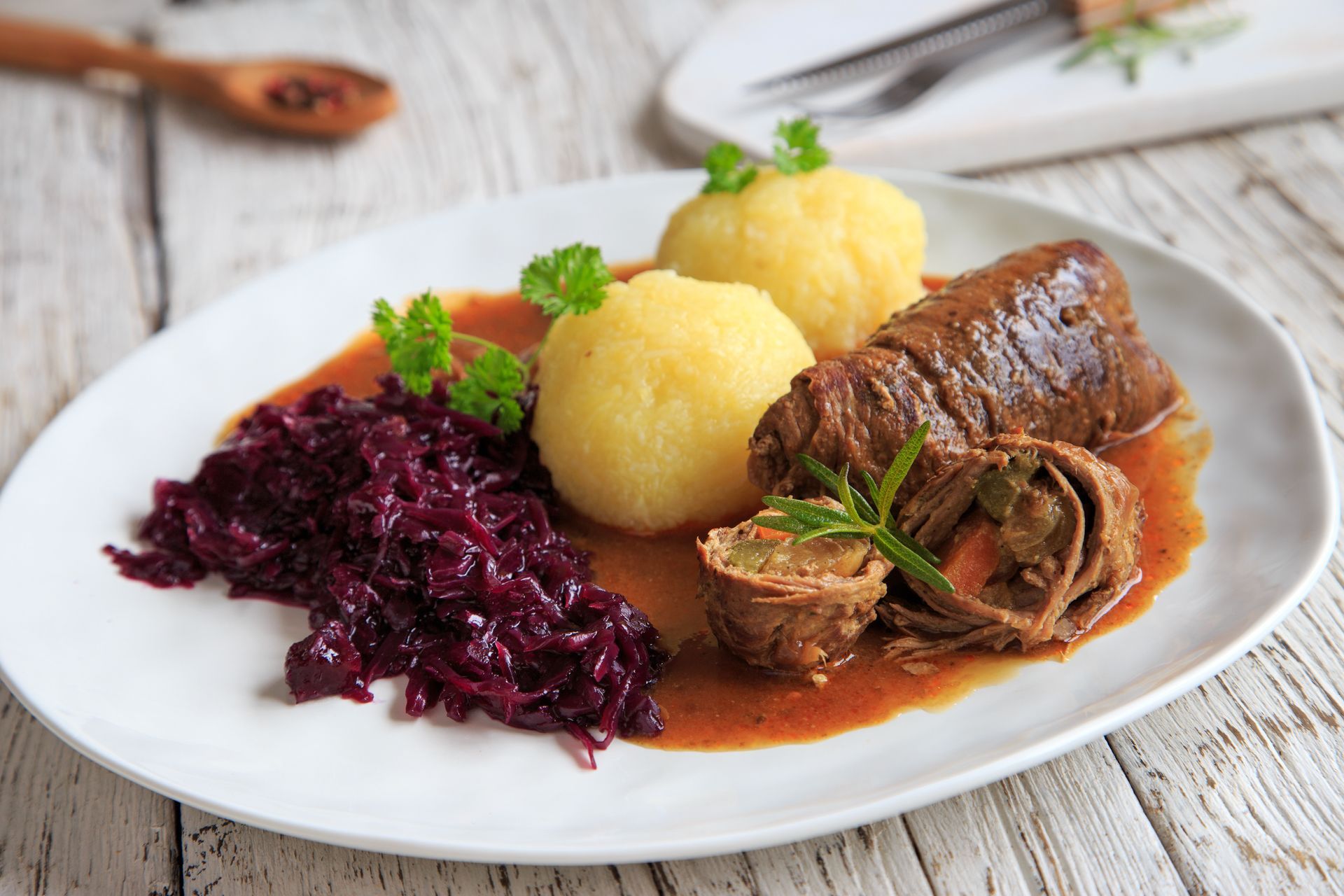 Teller mit deutschem Essen: Rindfleischröllchen, Kartoffelknödel und Rotkohl in Soße.