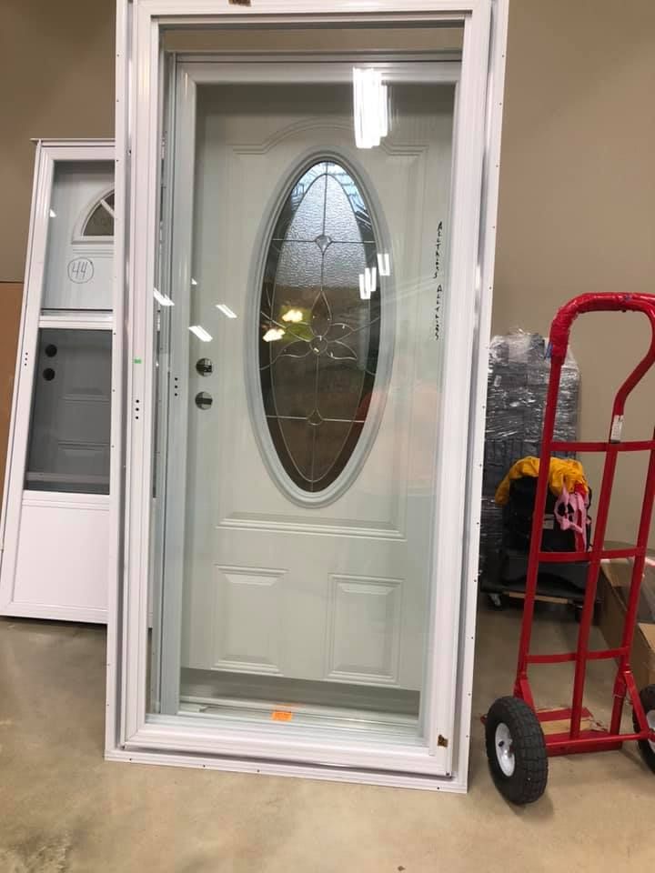 White door with oval glass and side screen, standing in a showroom. A red hand truck is in the foreground.