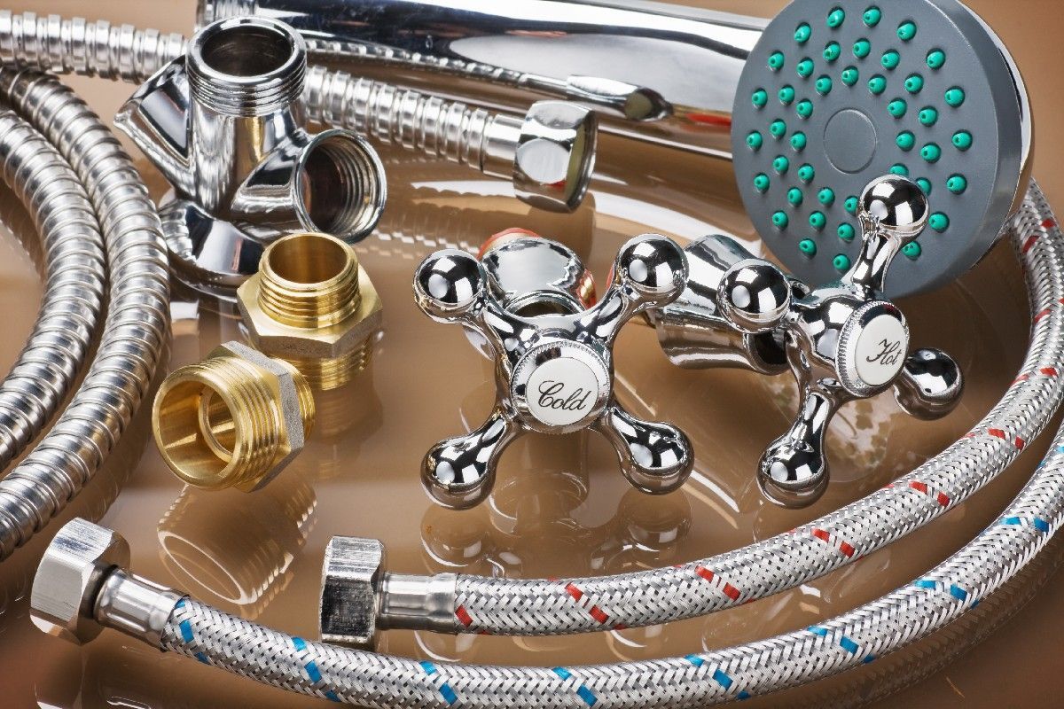 Chrome-finished shower fixtures and plumbing components, including hoses, valves, and showerhead, on a reflective surface.
