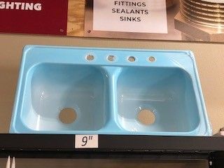 A light blue, double-basin sink with four faucet holes, sitting on a shelf.