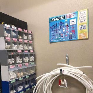 Shelves with plumbing fittings and a diagram on a wall, along with a roll of white tubing.