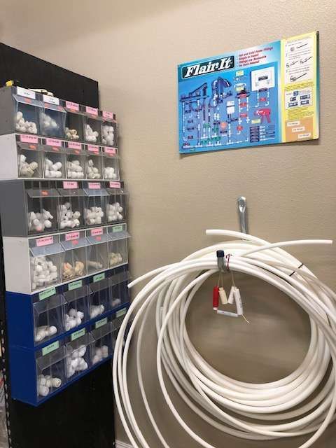 A storage rack with various plumbing fittings next to a coil of white tubing, under a 