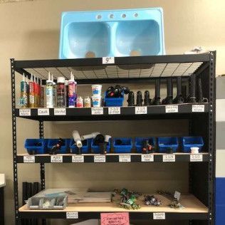 A shelf with plumbing supplies and a blue double sink in a store.