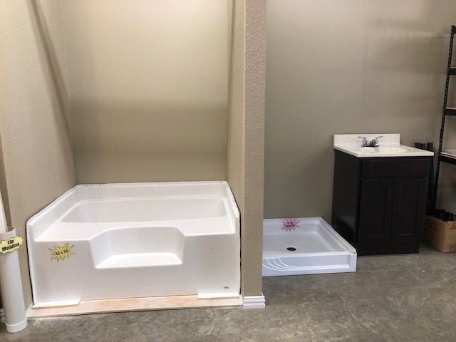 White walk-in shower unit with step and adjacent shower pan, vanity, in a room under construction.