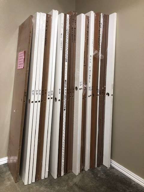 A stack of interior doors in varying wood tones and white, leaning against a wall in a room.