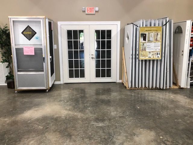 Display of doors in a hardware store: French doors, screen door, and a stack of white doors on a concrete floor.