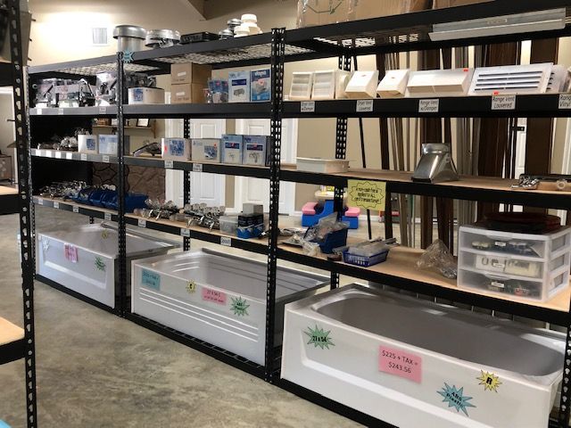 Shelves filled with plumbing supplies and bathroom fixtures in a retail store, with several white bathtubs displayed in front.